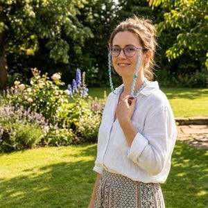 May include: A light blue beaded eyeglass chain featuring translucent, rounded links connected in a continuous loop. The chain is attached to the temples of a pair of glasses, with the beads displaying a soft, cool-toned color palette.