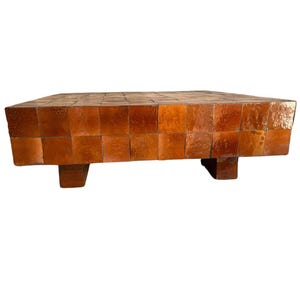 Peut inclure: Une table basse rectangulaire recouverte d'une grille de carreaux carrés brillants de couleur ambre. La surface et les côtés présentent un motif en mosaïque uniforme avec de légères variations de ton. La table repose sur quatre pieds courts.