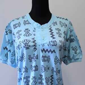 May include: A light blue short-sleeved shirt with a geometric pattern in black. The shirt has a button-up collar.