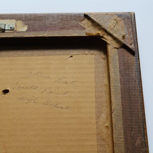 May include: A close-up of a wooden picture frame with a brown paper backing. The paper has handwritten text that reads "Steve Baker South Point High School".