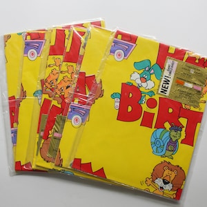 May include: A pack of five yellow wrapping paper rolls with a Happy Birthday theme. The paper features cartoon animals, a car, and the words "Happy Birthday" in red letters. The paper is packaged in clear plastic.