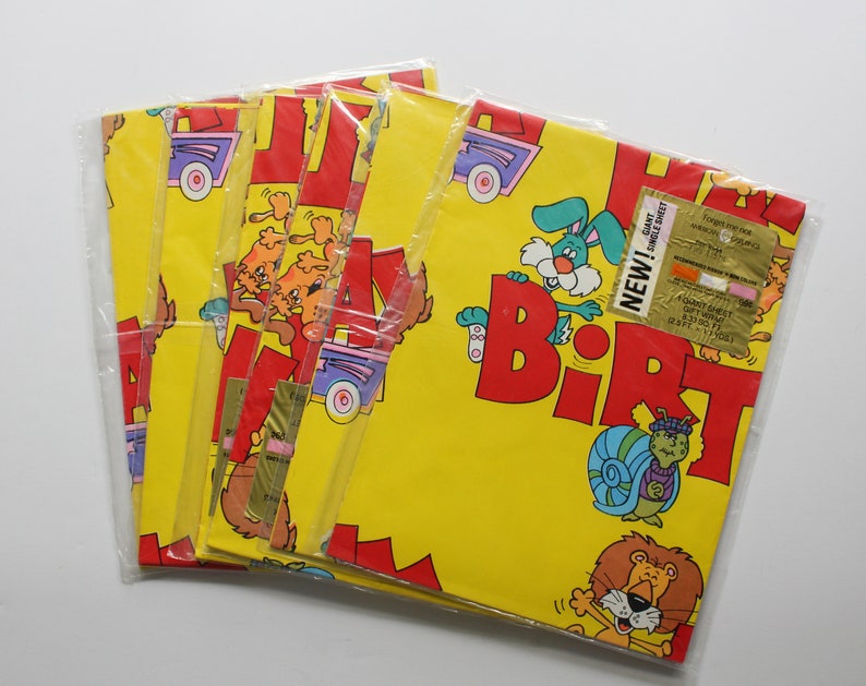 May include: A pack of five yellow wrapping paper rolls with a Happy Birthday theme. The paper features cartoon animals, a car, and the words "Happy Birthday" in red letters. The paper is packaged in clear plastic.