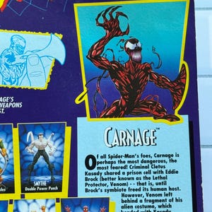 May include: A toy package featuring the character Carnage from the Spider-Man animated series. The package has a purple background with images of other characters and text. The Carnage figure is red with black accents.