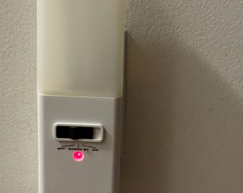 Könnte beinhalten: Ein weißes, bewegungsaktivierter Nachtlicht von Brinkmann mit einer roten LED-Anzeige. Das Licht hat einen Schalter mit den Beschriftungen "OFF", "STAND BY" und "ON".
