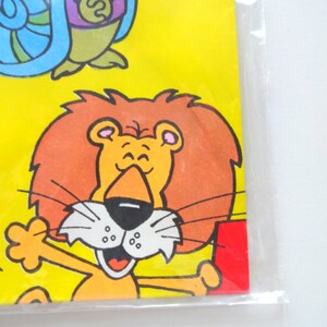 May include: A cartoon lion with a bright orange mane and a big smile. The lion is wearing a red shirt and has a yellow background.