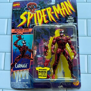 May include: A packaged Carnage action figure from the Spider-Man animated series. The red figure with black accents is displayed with weapon accessories. The packaging features the Spider-Man logo and text: "Exclusive Marvel T-Shirt Offer Inside!" The figure is in a plastic case.