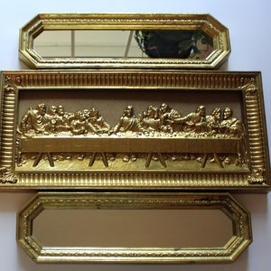 Puede incluir: Una pieza de arte de pared con marco dorado que representa la Última Cena. La obra de arte presenta un diseño en relieve tridimensional y está rodeada de un marco decorativo y ornamentado.