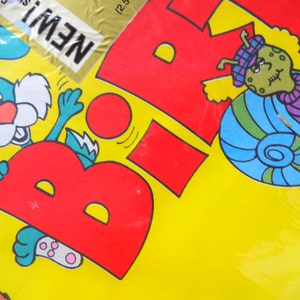 May include: A yellow background with a red letter "B" and a blue snail with a purple scarf. A green rabbit is holding onto the letter "B". The text "NEW!" is in the top left corner.