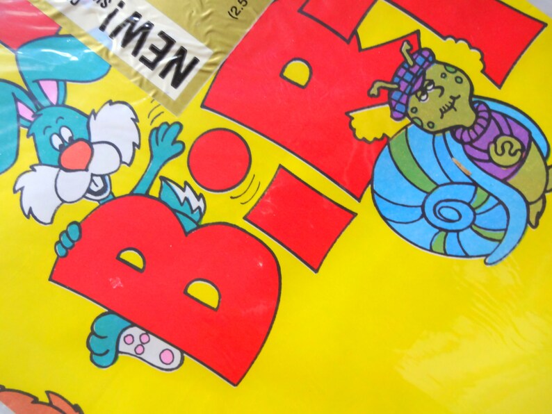 May include: A yellow background with a red letter "B" and a blue snail with a purple scarf. A green rabbit is holding onto the letter "B". The text "NEW!" is in the top left corner.