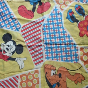 Könnte beinhalten: Vintage gelber Stoff mit Micky Maus, Minnie Maus und Pluto. Der Stoff hat ein Patchwork-Design mit geometrischen Mustern in Rot, Blau und Orange. Die Zeichentrickfiguren tragen ihre klassischen Outfits.