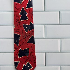 May include: A necktie featuring a vibrant red background with a repeating pattern of dark navy blue abstract triangular shapes and thin, intersecting black lines that create a dynamic, geometric visual effect across the entire length of the fabric.