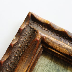 May include: Close-up of a corner of a wooden picture frame with a gold finish. The frame has a textured surface and a slightly raised edge.
