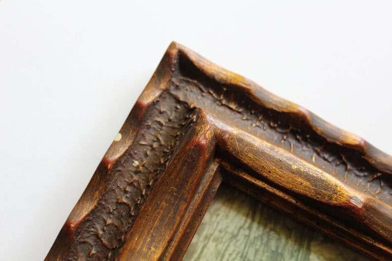 May include: Close-up of a corner of a wooden picture frame with a gold finish. The frame has a textured surface and a slightly raised edge.