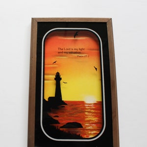 Może przedstawiać: Ramka z obrazem przedstawiającym zachód słońca z latarnią morską w cieniu na żółtym i pomarańczowym niebie. Na obrazie widnieje tekst "The Lord is my light and my salvation. Psalm 27:1".