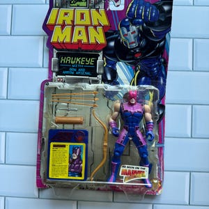 May include: A Hawkeye action figure from Marvel Comics, packaged on a colorful card. The figure is in a dynamic pose, with a bow and arrow. The packaging features the Iron Man logo and the text "Hawkeye with Bow and Arrow Arsenal."