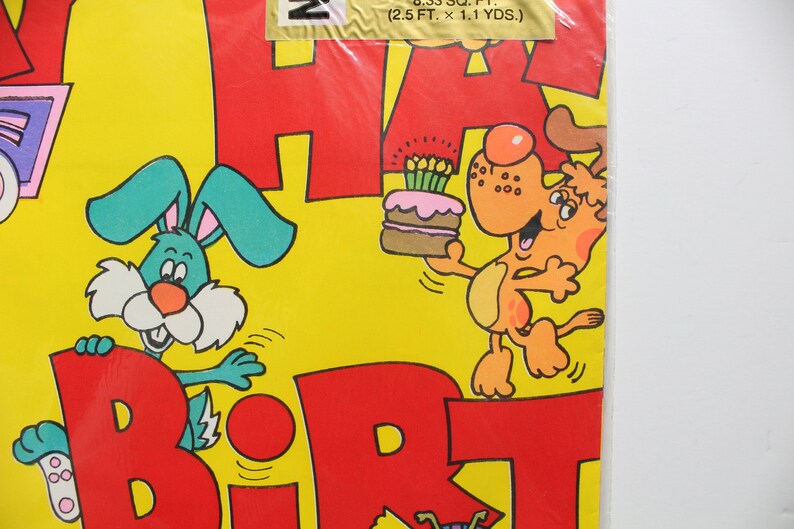 May include: A yellow, red, and green wrapping paper with a bunny and a dog holding a birthday cake. The paper says "Happy Birthday".