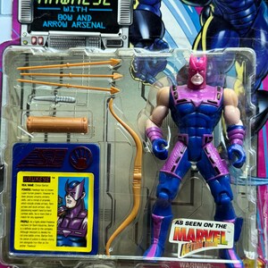 May include: Hawkeye action figure in original packaging. The figure is in a blue and purple costume, with a bow and arrow arsenal. The packaging features the text "Hawkeye with Bow and Arrow Arsenal" and "As Seen on the Marvel Action Hour".
