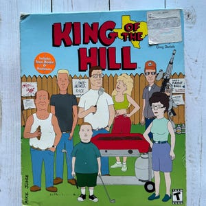 May include: A King of the Hill video game box cover featuring the main characters from the animated television series. The characters are depicted in a cartoon style, standing in front of a green lawn with a red grill and a propane tank. The title of the game is "King of the Hill" and the game is rated T for Teen.