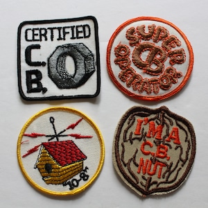 Könnte beinhalten: Vier gestickte Patches mit verschiedenen Designs. Der erste Patch ist weiß mit schwarzem Text, der "CERTIFIED CB" und eine graue Metallmutter sagt. Der zweite Patch ist orange mit braunem Text, der "SUPER OPERATOR" sagt. Der dritte Patch ist gelb mit einem weißen Haus mit einem roten Dach und Blitzen. Der vierte Patch ist braun mit orangefarbenem Text, der "I'M A CB NUT" sagt.