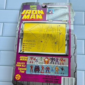 May include: The back of an Iron Man action figure package. The package features the Marvel Comics logo, the Iron Man logo, and a diagram of the figure's accessories. The package also includes a list of other figures to collect.