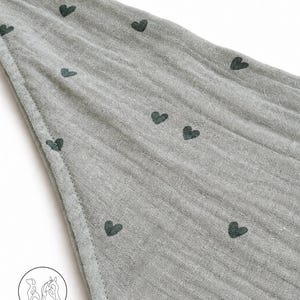 May include: A gray fabric with a pattern of dark green hearts. The fabric has a textured appearance and is stitched along the edge. The image is of a baby blanket or similar item.