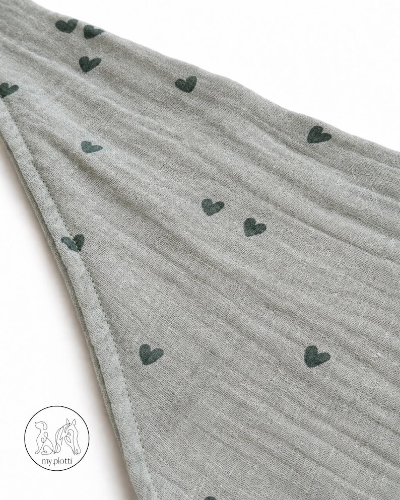 May include: A gray fabric with a pattern of dark green hearts. The fabric has a textured appearance and is stitched along the edge. The image is of a baby blanket or similar item.