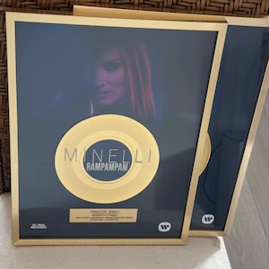 Könnte beinhalten: Eine goldgerahmte Auszeichnungstafel mit einer goldenen Schallplatte. Das mittlere Etikett zeigt den Text MINELLI RAMPAMPAM. Unter der Platte befindet sich ein goldenes Schild mit der Aufschrift SINGLE D'OR - REMIS À sowie Zertifizierungstext.