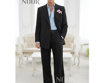 May include: A dark gray pinstripe suit with a light blue dress shirt and a pink flower in the lapel. The suit has a black belt and wide-leg pants. The word "NOOR" is printed in the upper left and lower right corners.