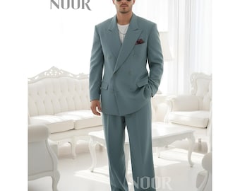May include: A light blue double-breasted suit with matching trousers. The suit features a classic design with a notched lapel and a pocket square. The image includes the text "NOOR" in the upper left and lower right corners. The person is wearing white sneakers.