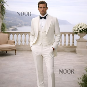 May include: A formal ivory suit with a matching vest and trousers, paired with a black bow tie. The suit features a tailored fit and is worn by a person standing outdoors. The word "NOOR" is displayed in the image.