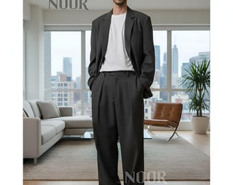 May include: A charcoal gray suit, consisting of a blazer and wide-leg trousers, paired with a white t-shirt and white sneakers. The word "NOOR" is printed at the top and bottom of the image. The suit is worn by a person standing in a modern living room.