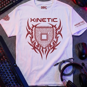 Peut inclure: T-shirt blanc avec un motif graphique rouge. Le motif comprend le mot "KINETIC" au-dessus d'un circuit imprimé en forme de bouclier. Le texte "KINETIC // OVERCLOCK" est sur la manche. Des accessoires de jeu entourent le t-shirt.