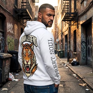 Pode incluir: Moletom branco com um gráfico de tigre nas costas, com o texto "URBAN LEGEND" acima do tigre e "STREET SOUL" na manga. O tigre é laranja, marrom e creme. O moletom é usado em um beco urbano.