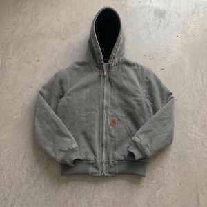Puede incluir: Una chaqueta con capucha en color verde salvia desteñido, con cremallera frontal completa, puños y dobladillo acanalados y forro interior negro. Un pequeño parche rectangular beige con el logo de Carhartt está cosido en el bolsillo.