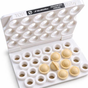 Può includere: Un utensile in plastica bianca JP MiniMidiMax Advanced Press Baby con coperchio incernierato dotato di rientranze circolari. La base contiene diversi scomparti circolari, alcuni dei quali contengono piccoli alimenti beige a cupola.