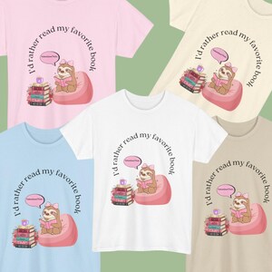 Puede incluir: Varias camisetas de diferentes colores, cada una con un perezoso de dibujos animados leyendo un libro en un puf. El texto "I'd rather read my favorite book" está en arco. Las camisetas son rosas, blancas, azules y beiges.