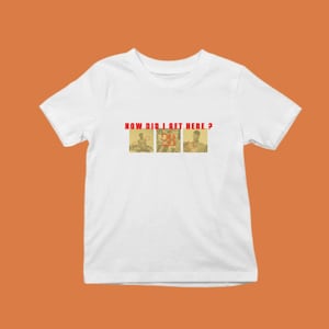 Può includere: T-shirt bianca con la scritta rossa "HOW DID I GET HERE ?" sopra tre piccole immagini. Le immagini sembrano essere fotografie d'epoca di persone in varie pose. La maglietta è presentata su uno sfondo arancione.