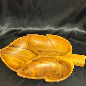 May include: A wooden leaf-shaped serving tray with three compartments. The tray is made of light brown wood and has a smooth, polished finish. The handle extends from the side. Ideal for serving snacks or appetizers.