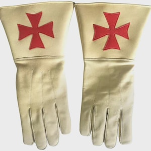 Puede incluir: Un par de guantes color crema con un emblema de cruz de Malta rojo en el gauntlet. Los guantes están hechos de un material liso y tienen costuras detalladas a lo largo de los dedos y la parte posterior de la mano. Los guantes parecen nuevos.