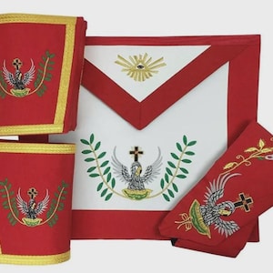 Puede incluir: Un conjunto de insignias ceremoniales rojas y blancas, que incluye un delantal y brazaletes. El delantal es blanco con un borde rojo y presenta un diseño bordado de una cruz, un águila y ramas de laurel. Los brazaletes son rojos con ribete dorado y bordados similares.
