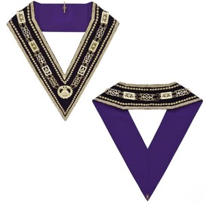 Puede incluir: Dos collares ceremoniales. Uno es de color púrpura oscuro con un borde negro, adornado con eslabones de cadena dorados, perlas y un emblema central. El segundo collar tiene un diseño similar, pero con un reverso púrpura liso.