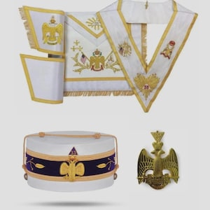 Puede incluir: Un conjunto de objetos ceremoniales blancos y dorados, que incluyen un delantal, un collar y un sombrero. El delantal y el collar presentan bordados y flecos dorados. El sombrero tiene una banda morada con detalles dorados. También hay un emblema dorado.