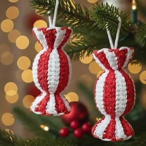 Può includere: Due decorazioni natalizie fatte a mano a forma di caramella, con strisce rosse e bianche. Gli ornamenti sono all'uncinetto e appesi a fili bianchi su un albero di Natale. Lo sfondo ha luci sfocate.