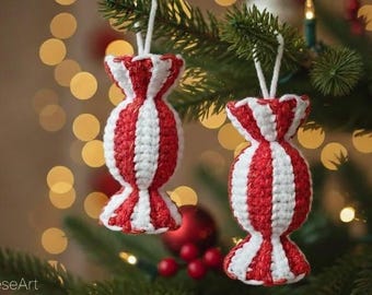 Puede incluir: Dos adornos navideños hechos a mano con forma de caramelo, con rayas rojas y blancas. Los adornos están hechos a ganchillo y colgados de cuerdas blancas en un árbol de Navidad. El fondo tiene luces borrosas.
