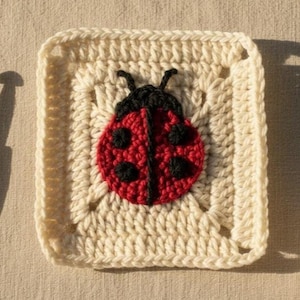 以下が含まれることがあります： 中央に赤いテントウムシのデザイン、黒い水玉模様と黒い頭が付いた、正方形のオフホワイトのかぎ針編み作品。 正方形にはテクスチャード加工のボーダーがあります。 かぎ針編みの作品は詳細で、色は鮮やかです。