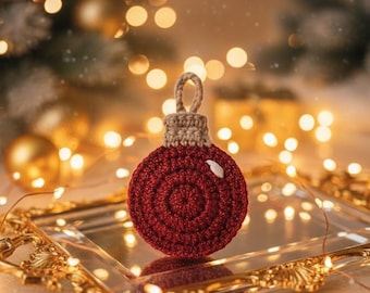 May include: A handcrafted, red crocheted Christmas ornament with a spiral design. The ornament has a tan top and a loop for hanging. It is displayed on a gold-framed mirror with blurred fairy lights in the background, creating a festive holiday scene.