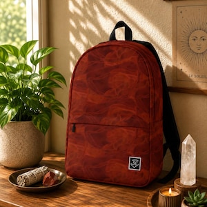 May include: A red backpack featuring a swirling smoke-like pattern throughout the fabric. The bag includes black shoulder straps, a top handle, and a small rectangular white patch on the lower front corner with the black text 3E inside a shield.
