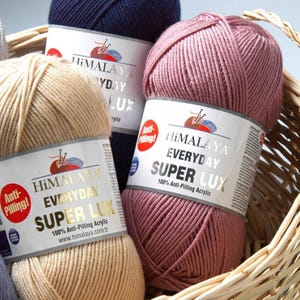 May include: Close-up of several yarn skeins in a woven basket. The yarn is in various colors, including beige, navy blue, and mauve. Each skein has a label that reads "Himalaya Everyday Super Lux 100% Anti-Pilling Acrylic."