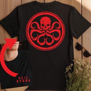 Bold red circular Hydra emblem on black featuring a stylized skull with a distressed texture, at the top with four segmented tentacles curling outward and downward into circular suction-cup tips, enclosed within a double red ring border, in a clean two-color graphic design.

Front design says the iconic Hydra salute "HAIL HYDRA" in distress lettering.