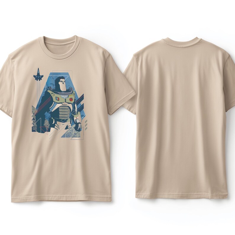 May include: A beige short-sleeved t-shirt featuring a graphic print of a space ranger character in a white, green, and purple suit. The design includes geometric blue shapes and a small rocket ship icon. The back of the t-shirt is plain beige.